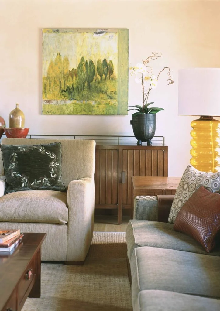 A glimpse at a corner of a living room where two sofas are corned by an end table. The sofas are taupe with throw pillows. A gold accent lamp sits on the table.