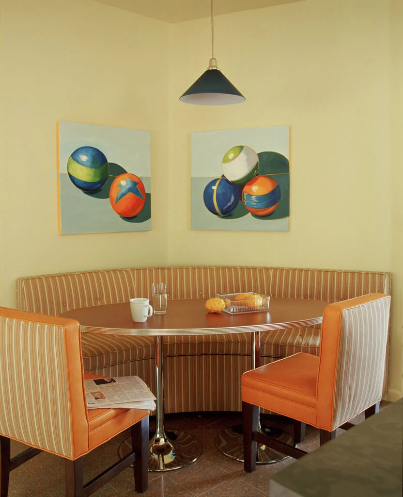 A small dining room with an upholstered banquette and two upholstered chairs around a retro oval table.
