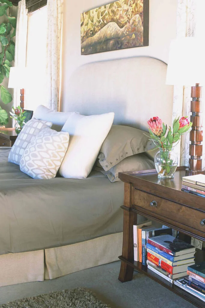 A bedroom in olive green and white. The bed has a pile of throw pillows. The bedroom is not a good place to work from home.