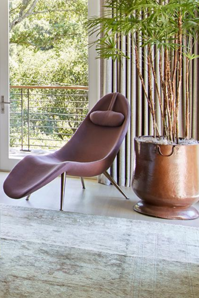 A dusty pink chaise lounge beside a large barrel planter. A chaise is timeless whether it is contemporary, like the one pictured, or more traditional.
