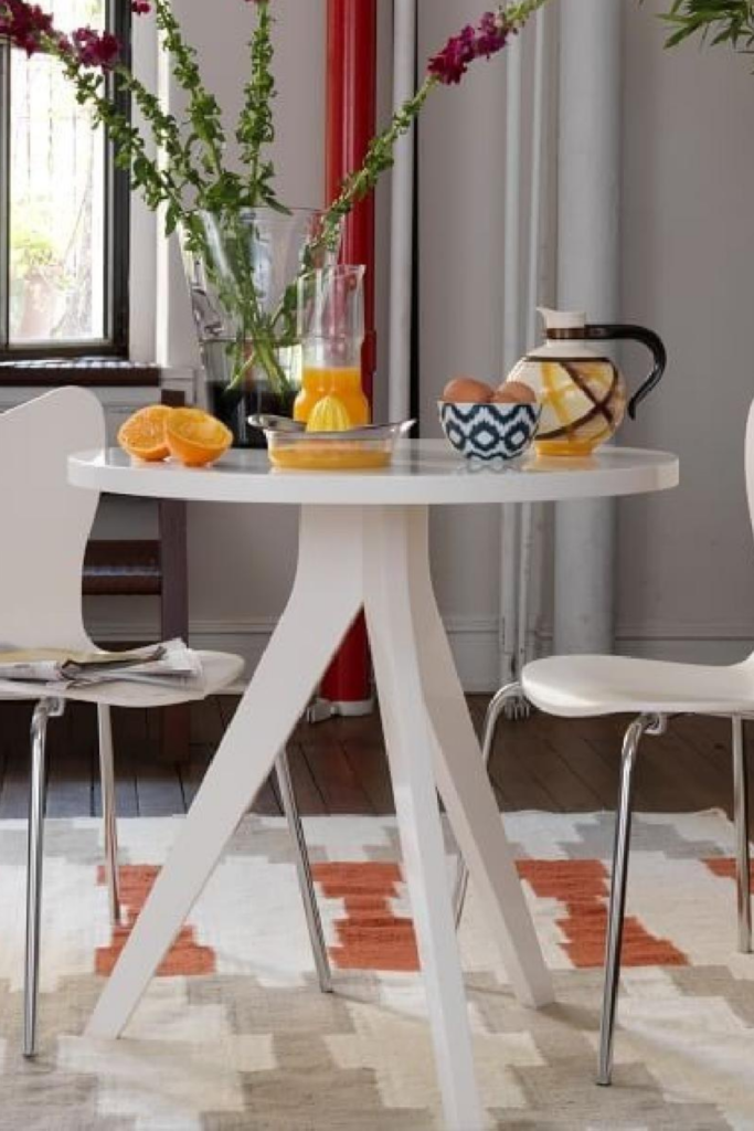 A white tripod table is flanked by two chairs. It is the perfect statement of minimalism and timeless.