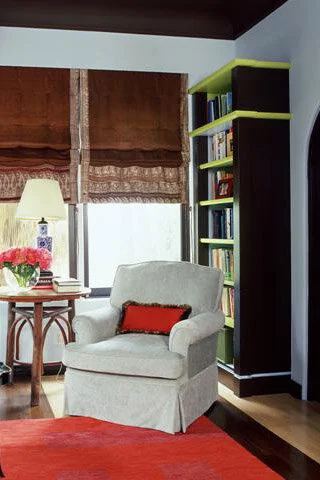 A white comfortable chair with a red pillow sits in front of a bookcase that is painted black with lime green accents. A holiday refresh can be achieved by painting a room.